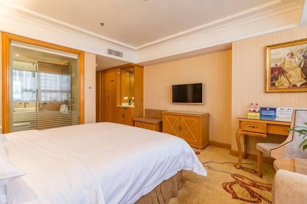 A hotel room with a large bed, a desk, a television, and a painting on the wall.