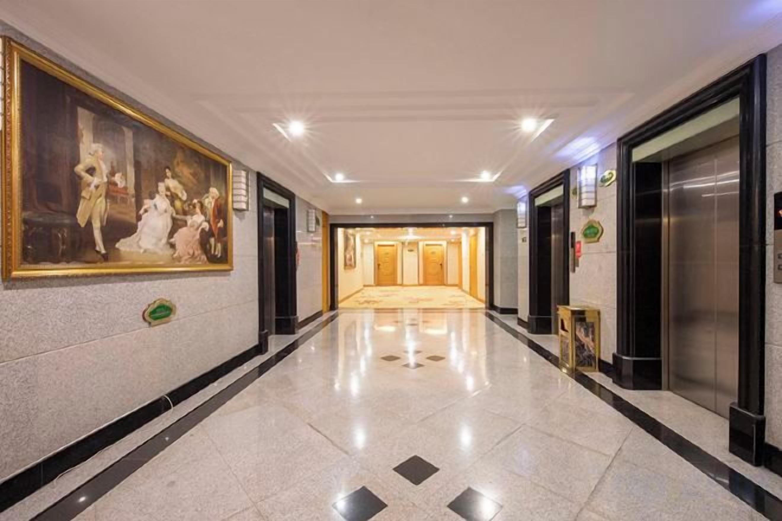 A hotel corridor with a large classical painting on the wall, a carpeted floor, and a reception area in the distance.