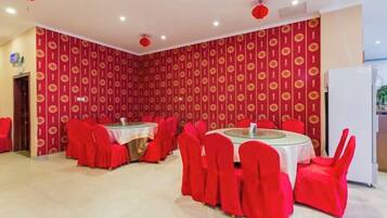 Un espace repas avec des tables rondes et des chaises rouges, un mur orné de motifs et un réfrigérateur blanc.