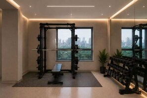 A gym with a squat rack, bench, and dumbbells, a large window with a city view, and a mirror reflecting the equipment. - Vienna International Hotel (Beijing Niujie Guang'anmennei Subway Station Branch) (Beijing)