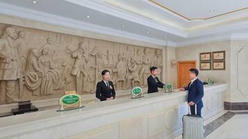 A reception desk with three staff members, a marble wall with relief sculptures, and a wooden door.