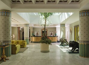 A lobby with a reception desk, a large central plant, and a statue of a lion.