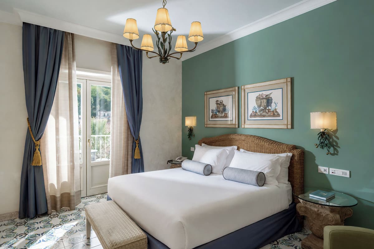 Hotelkamer met een bed, een bankje, een ronde tafel, een stoel, een kroonluchter en twee wandlampen.