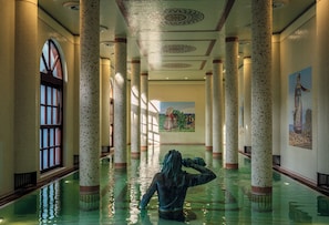 A large indoor pool with columns, a mural, and a statue.