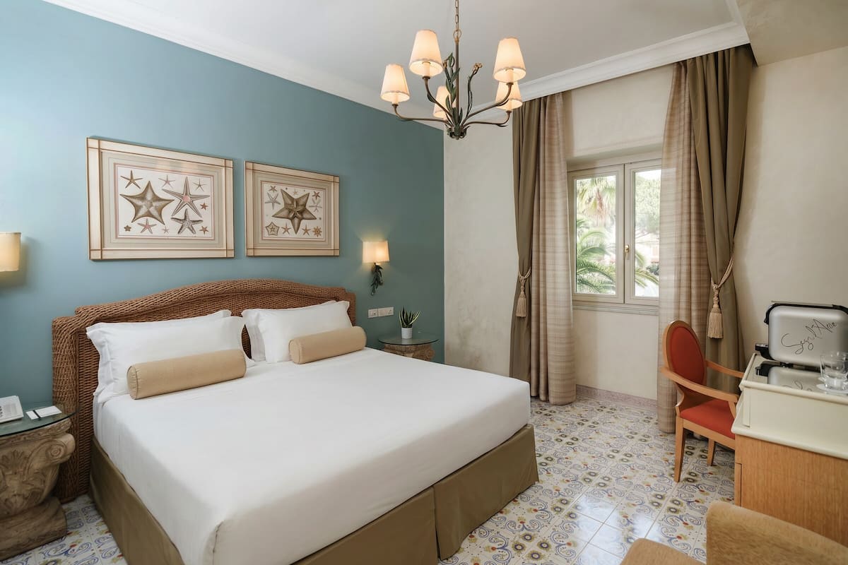Hotelkamer met een groot bed, een bureau, een stoel, een kroonluchter en twee sterdecoraties in lijsten aan de muur.
