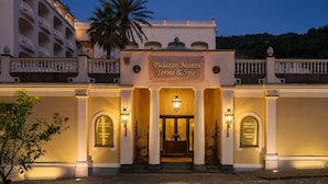 Een hotelentree met een bord waarop 'Palazzo Manzi Terme & Spa' staat, met een boogvormige deuropening, kolommen en een palmboom.
