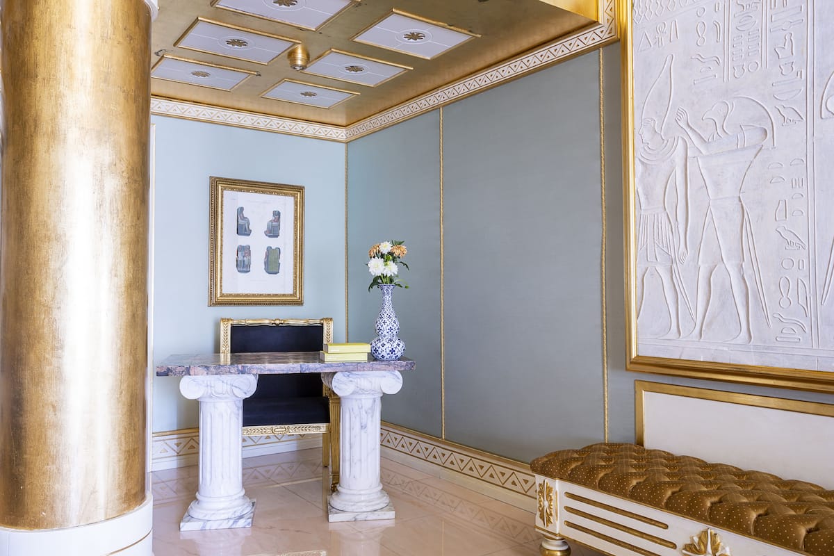 Een kamer met een marmeren schoorsteen, een ingelijst schilderij aan de muur en een vaas met bloemen.