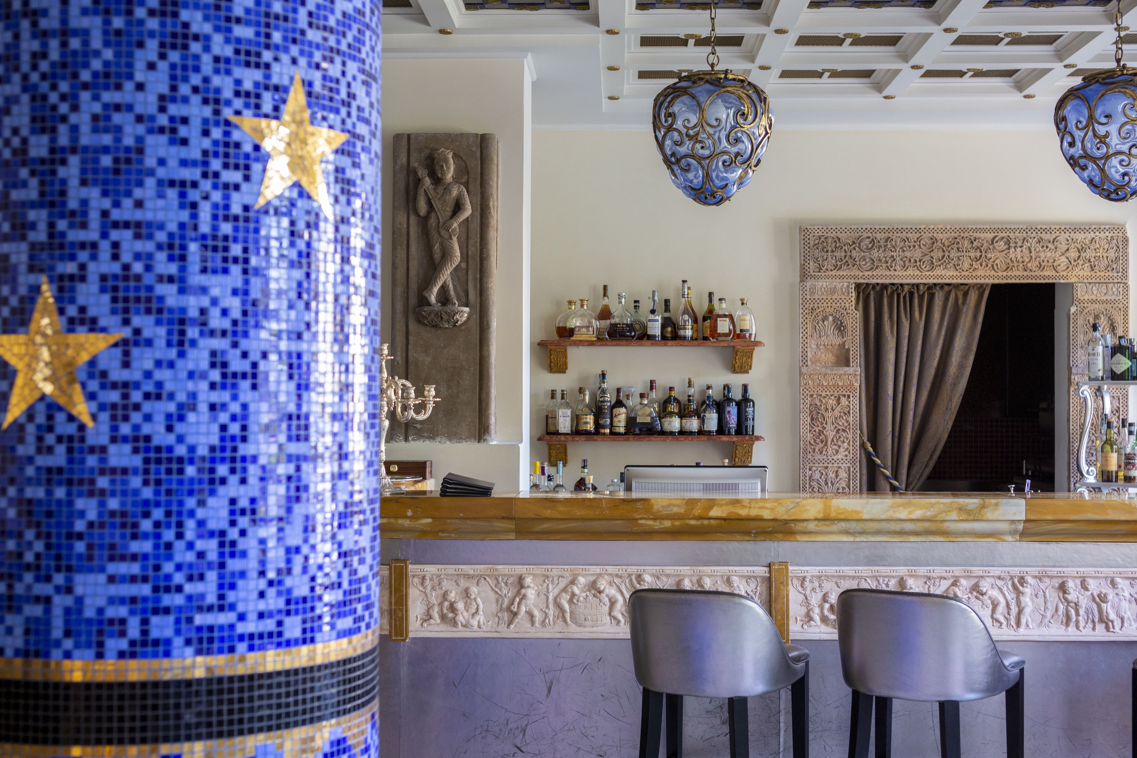 Angolo bar con colonna a mosaico, sgabelli da bar, scaffali con bottiglie e decorazioni elaborate al soffitto.