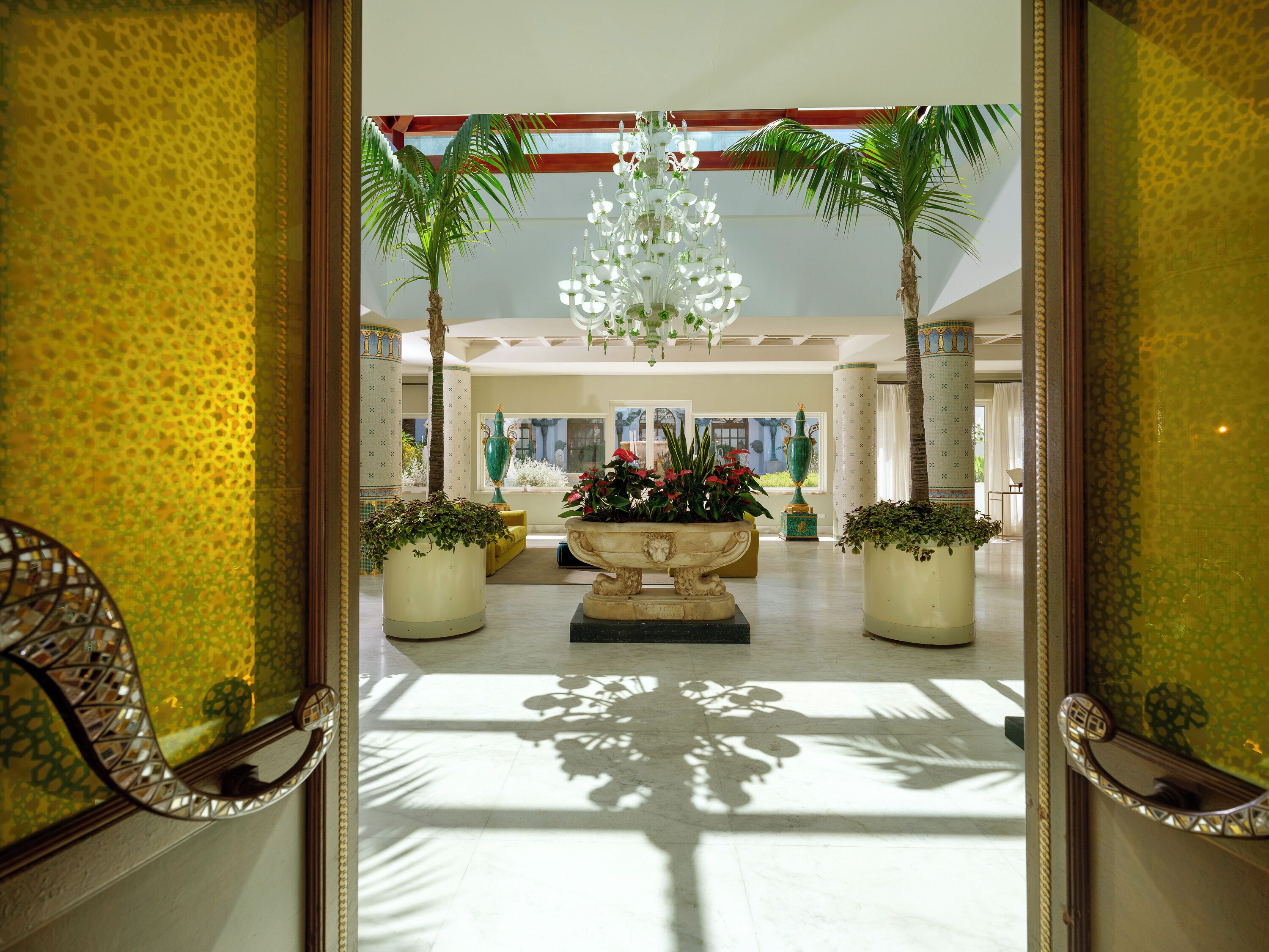 A lobby with a central fountain, potted plants, and a chandelier.