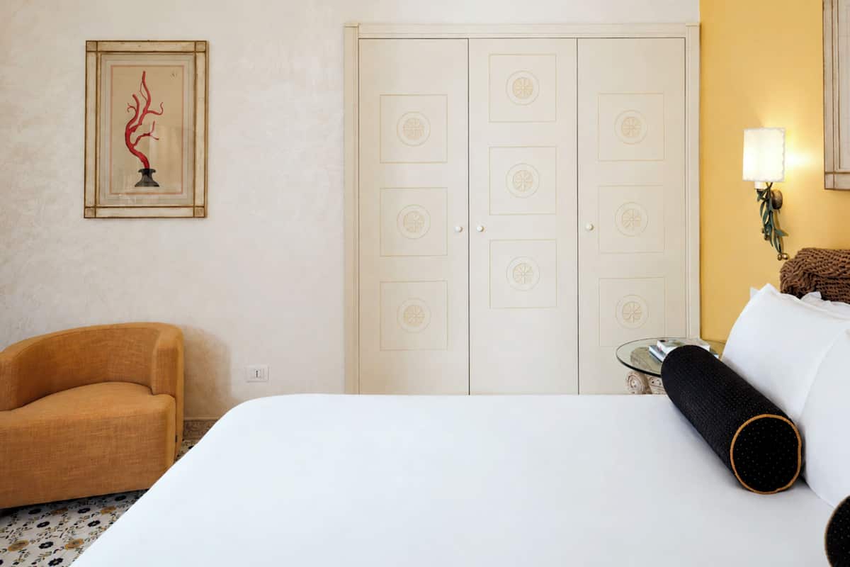 Een hotelkamer met een bed, een stoel, een lijst met kunstwerk, een garderobe en een lamp.