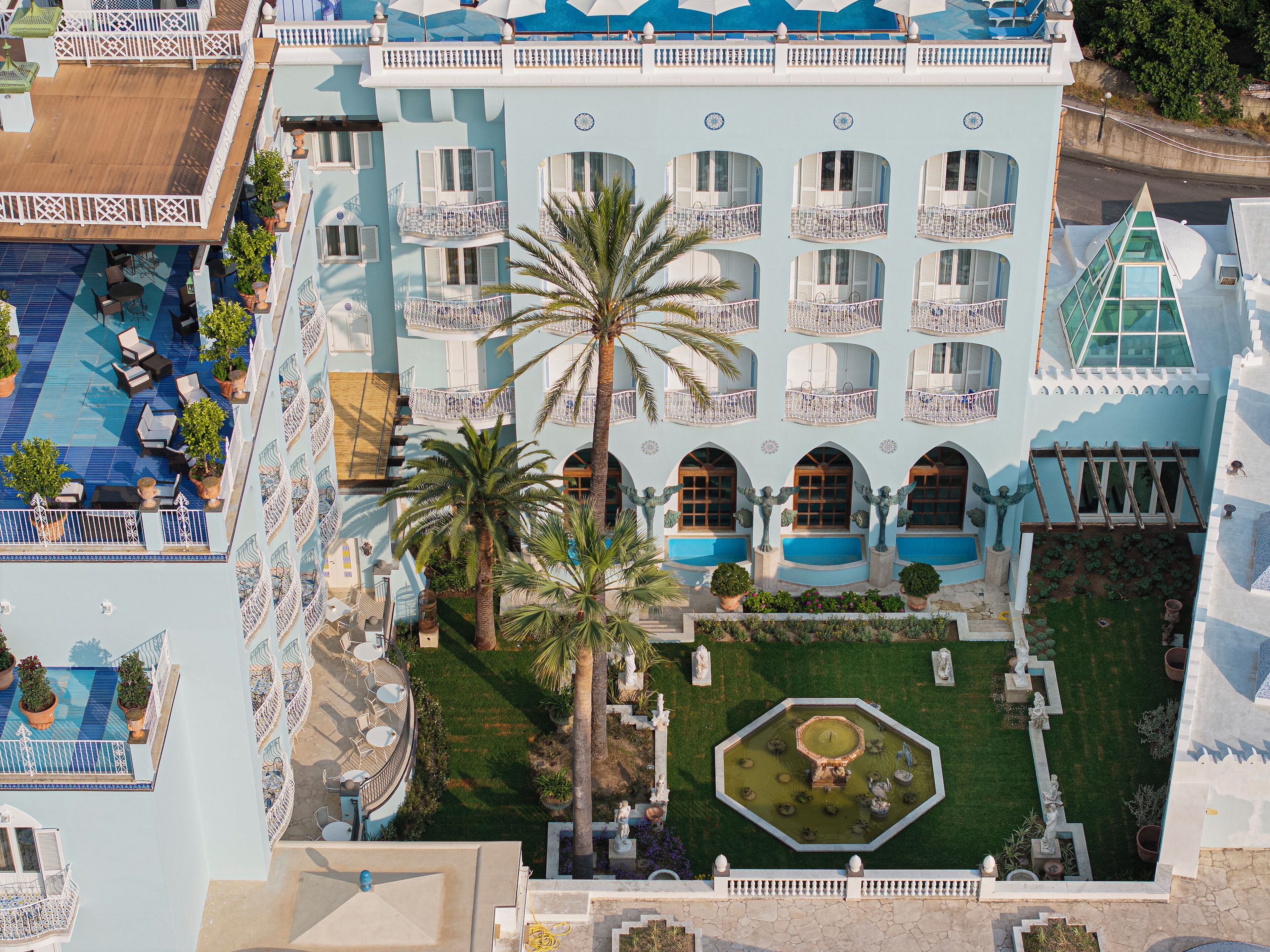 Een hotel met meerdere verdiepingen, балконы, zwembad en een centrale binnenplaats met beelden en een fontein.