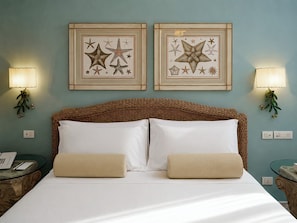 A neatly made bed with two pillows, a wicker headboard, two framed starfish wall art pieces, and two wall-mounted lamps. - Palazzo Manzi Terme & Spa   (Casamicciola Terme)