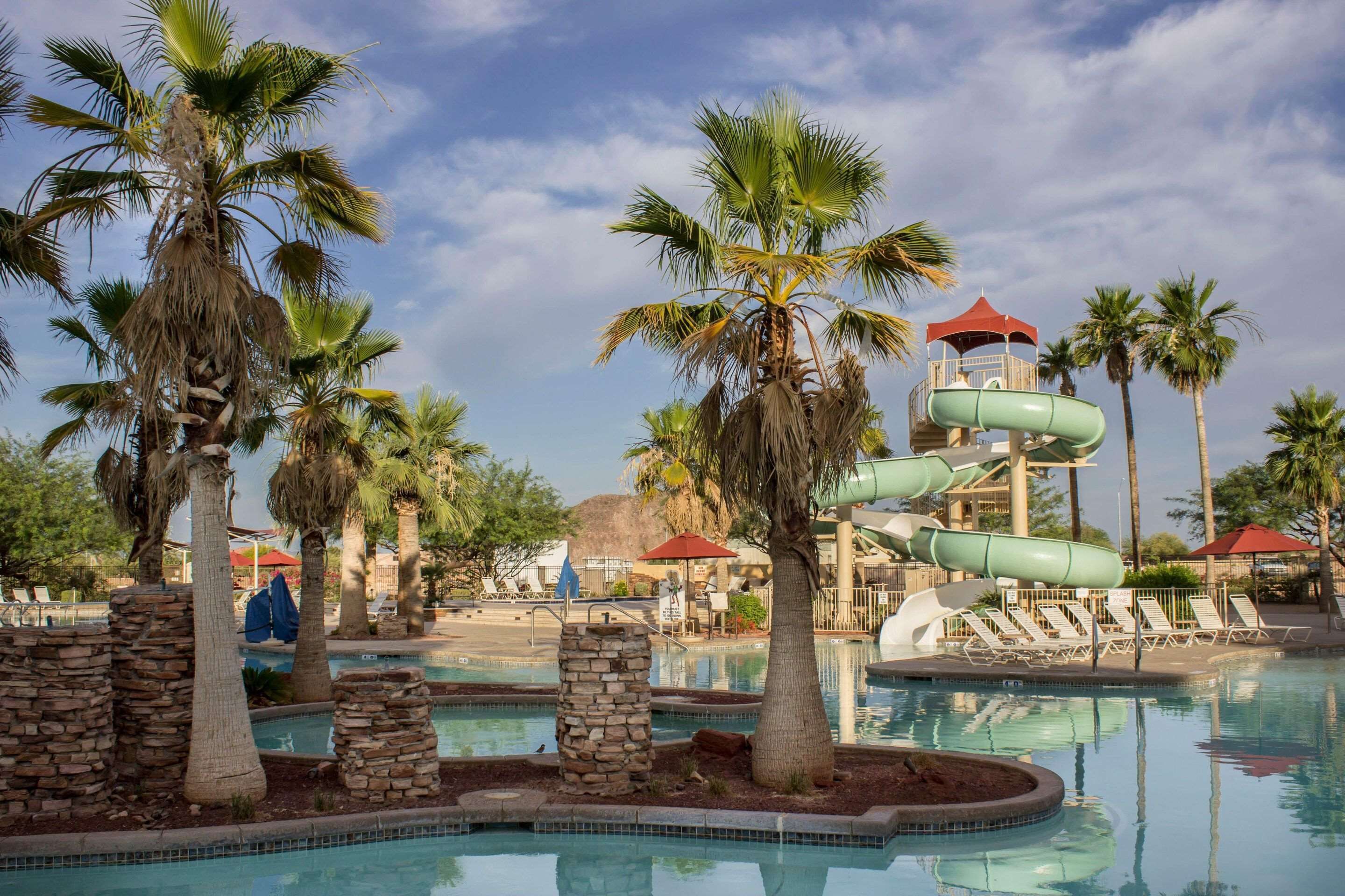 A pool area with palm trees, a water slide, and lounge chairs.
