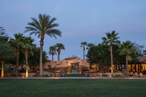 A desert-style building with a stone facade, palm trees, and a well-maintained lawn.