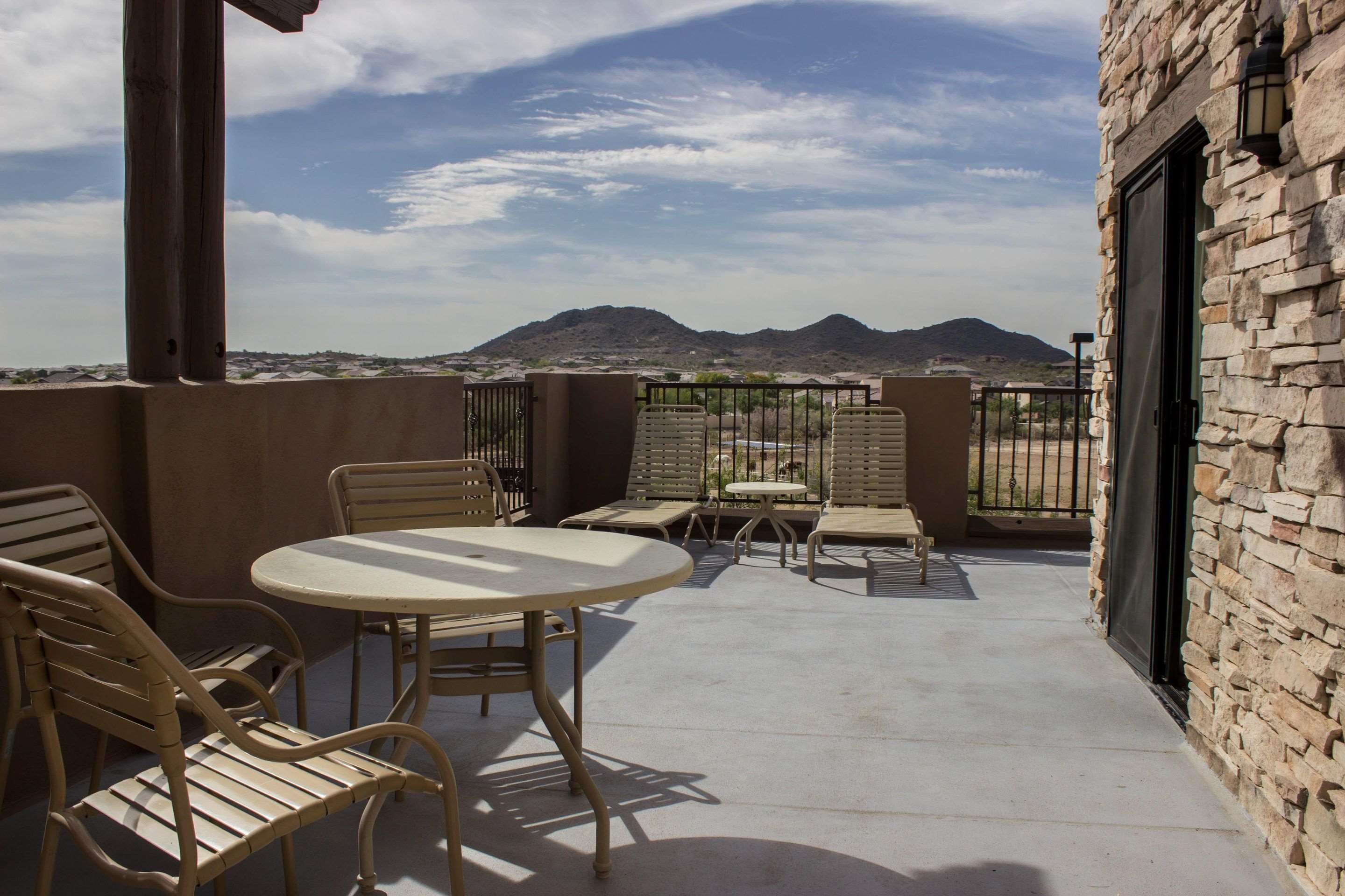 A balcony with a table and chairs, a stone wall, and a view of distant mountains.