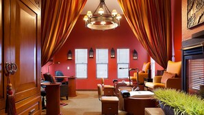Ein gemütlicher Dachbodenraum mit roter Wand, einer Chandelierleuchtre und einem Kamin. Es gibt zwei Fenster mit Jalousien, einen Schreibtisch und einen Stuhl.
