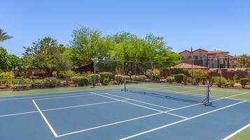 A tennis court with a net, surrounded by a fence and various plants.