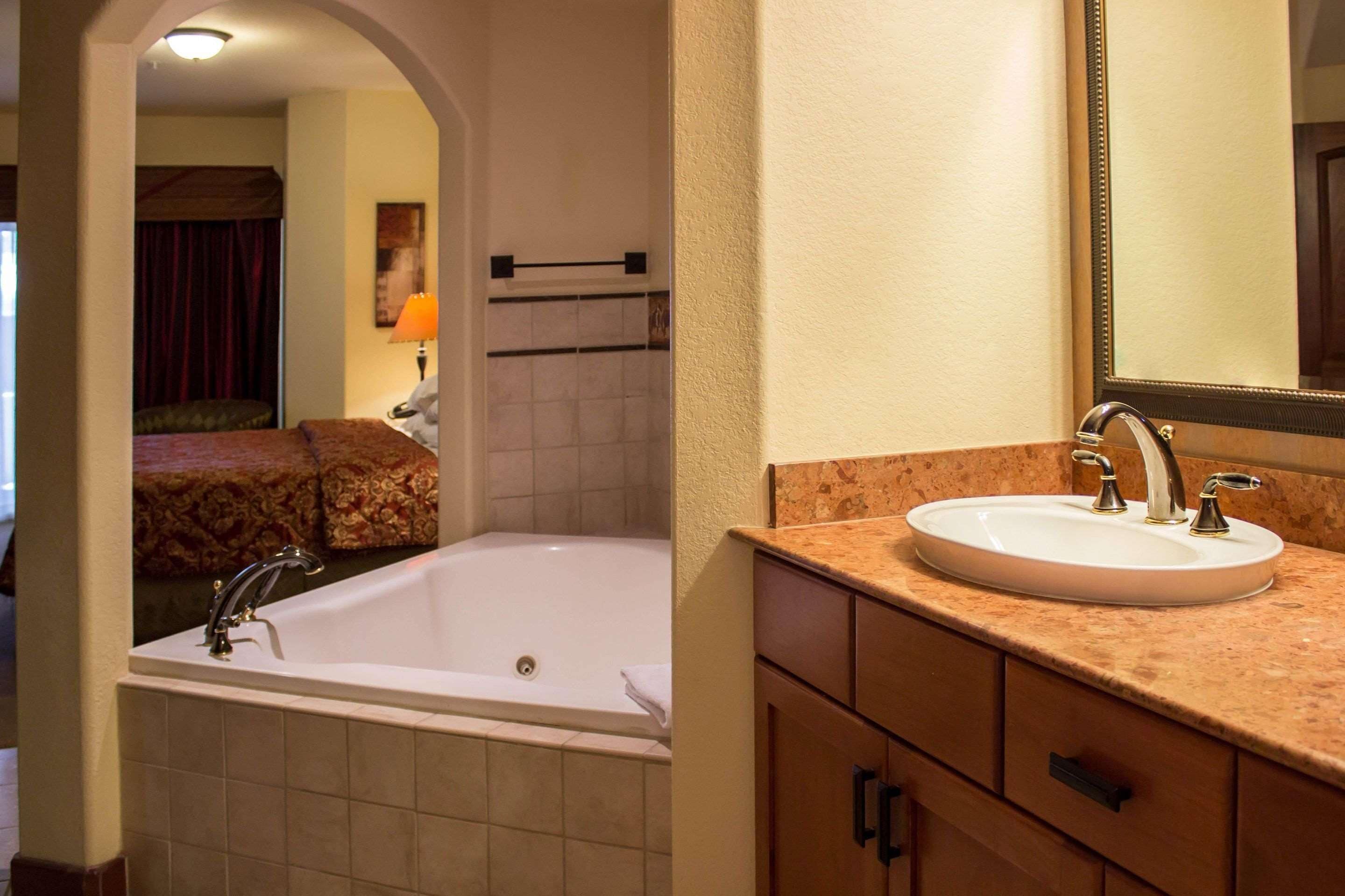 Un baño con una bañera blanca, un lavabo con dos grifos y un espejo sobre el lavabo.