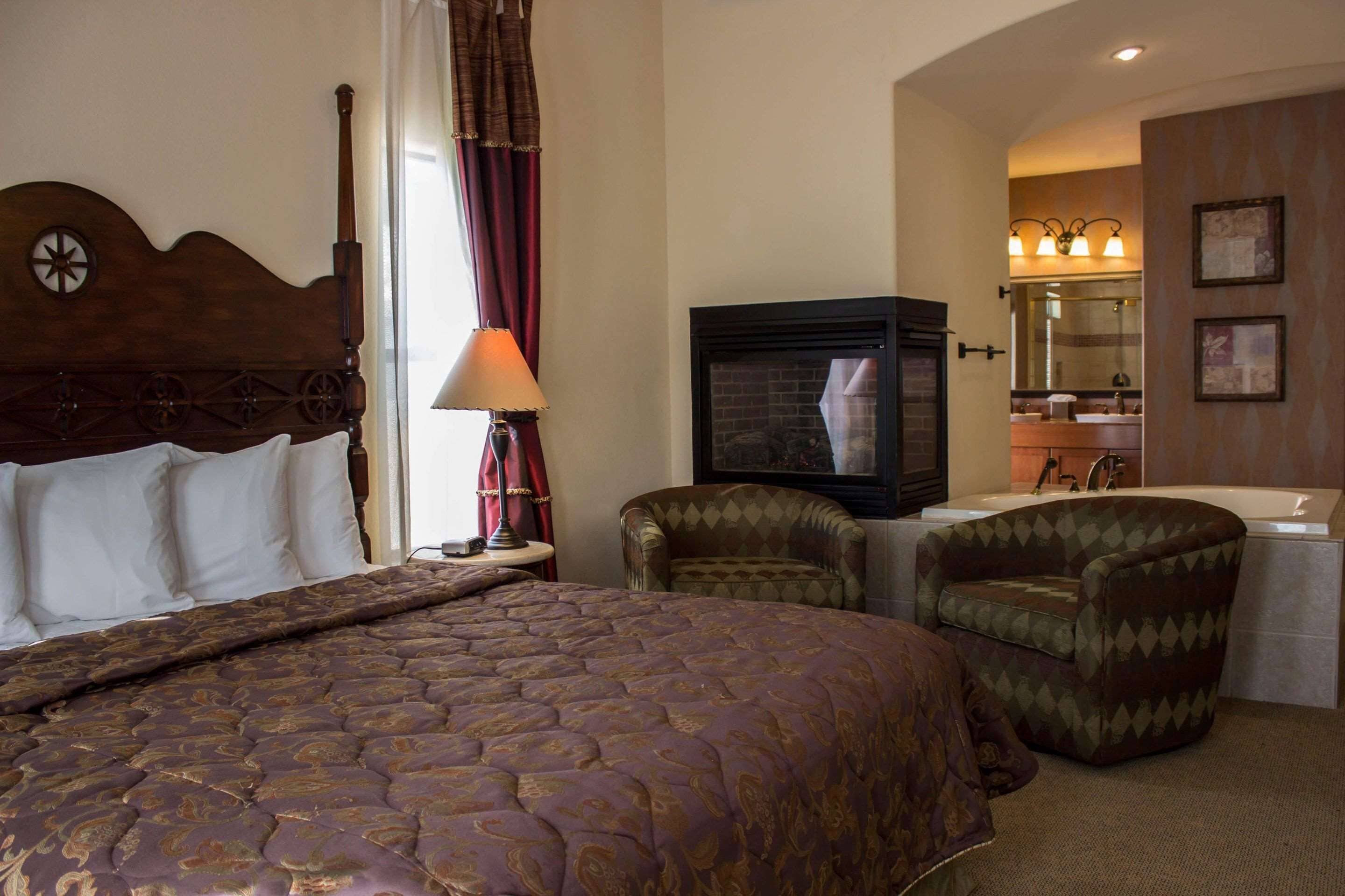 A hotel room with a large bed, a television, a chair, and a bathroom with a sink and mirror.
