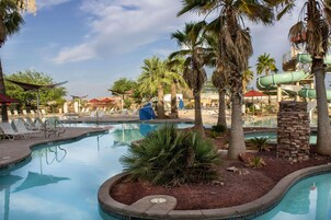 A pool area with lounge chairs, palm trees, and a water slide.