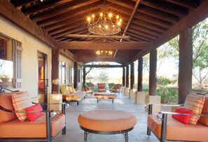 Un espacio de estar al aire libre techado con un candelabro, asientos acolchados y vistas al exterior.