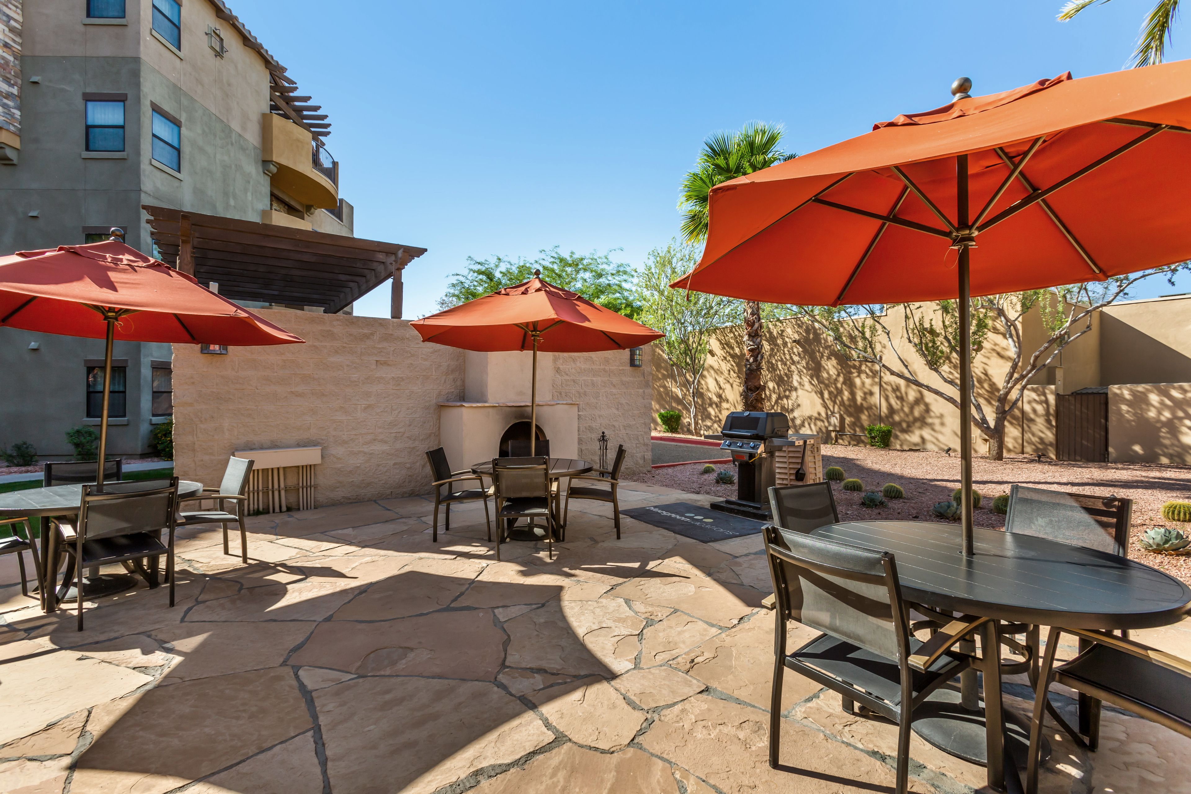 Un espace extérieur aménagé en terrasse, avec un sol en pierre, plusieurs tables et chaises, et des parasols rouges.