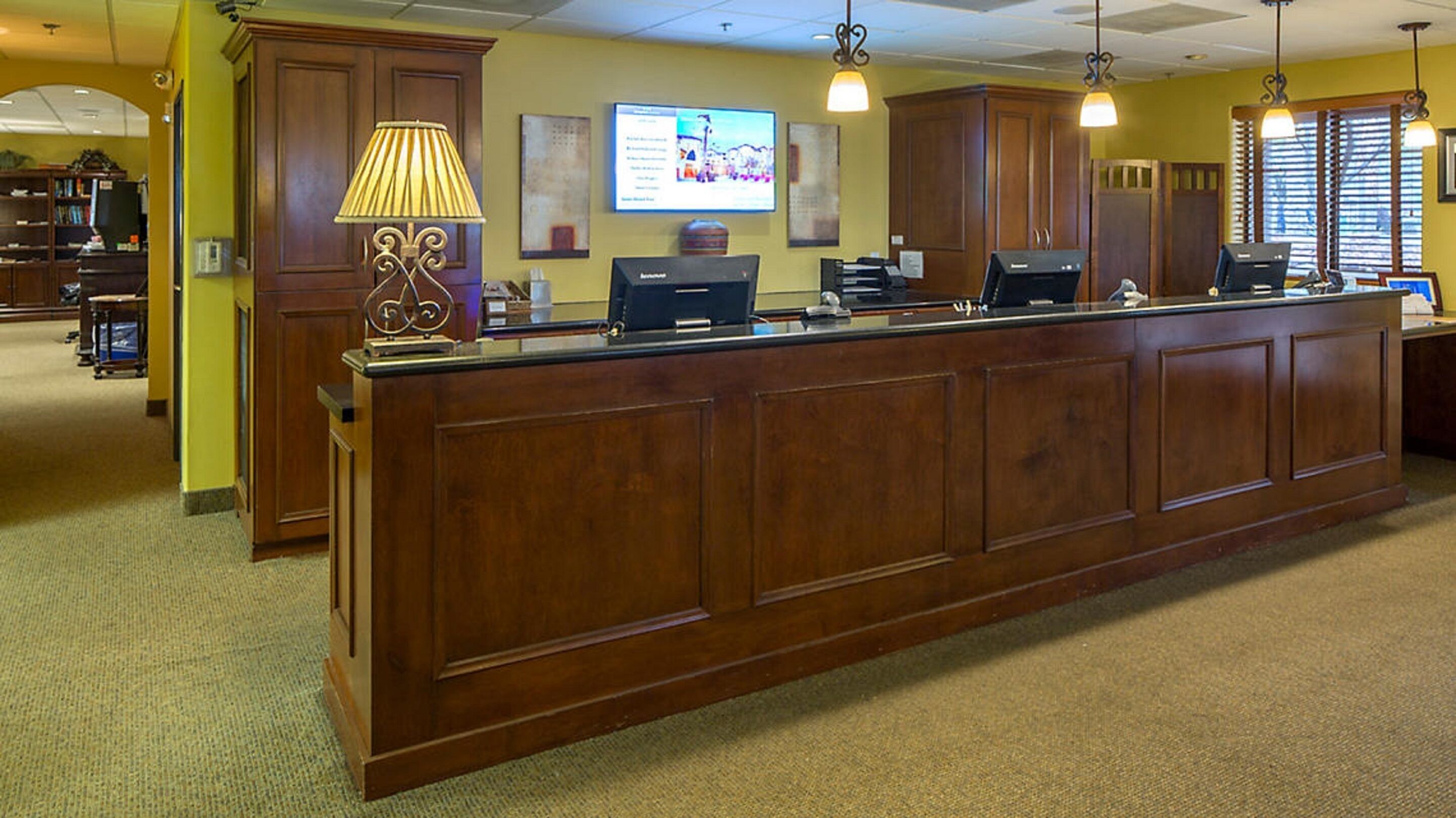 A reception desk with a computer, a lamp, and a TV screen in a hotel lobby.