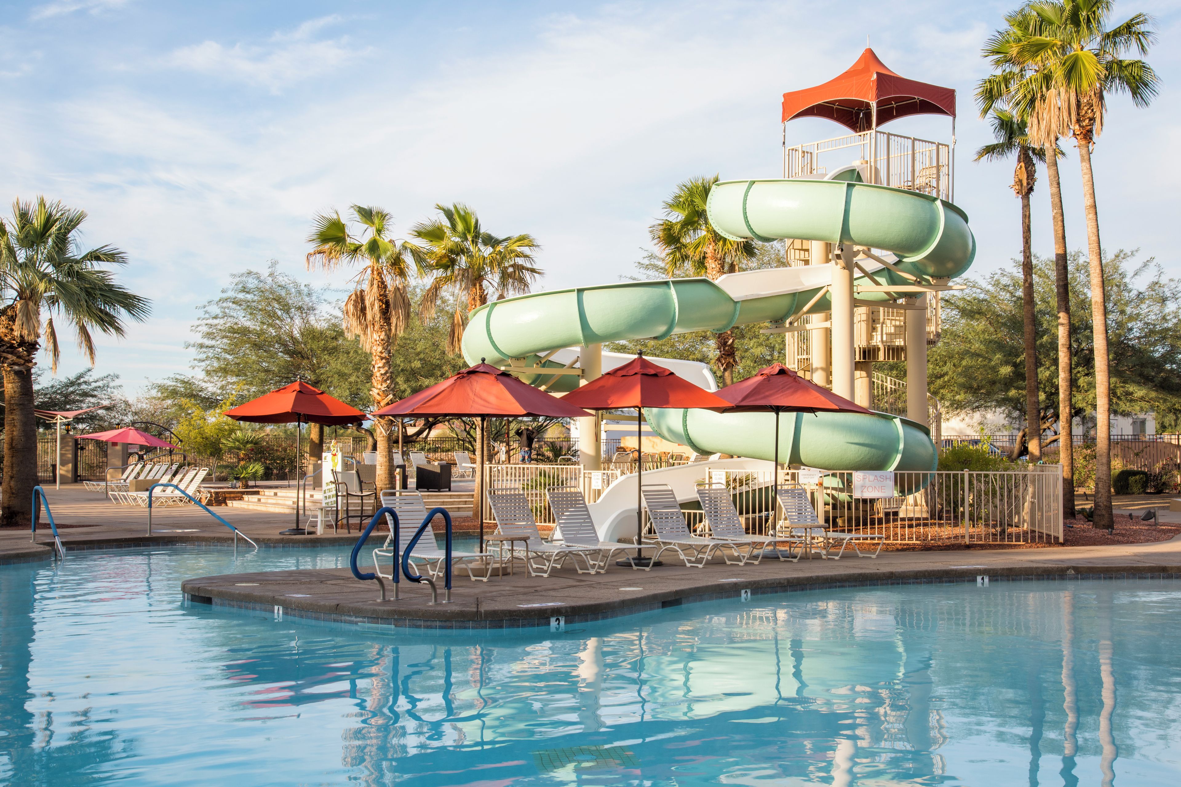 A pool area with a water slide, lounge chairs, and umbrellas.