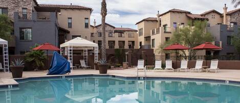 A swimming pool with lounge chairs and umbrellas, surrounded by multi-story buildings with balconies.