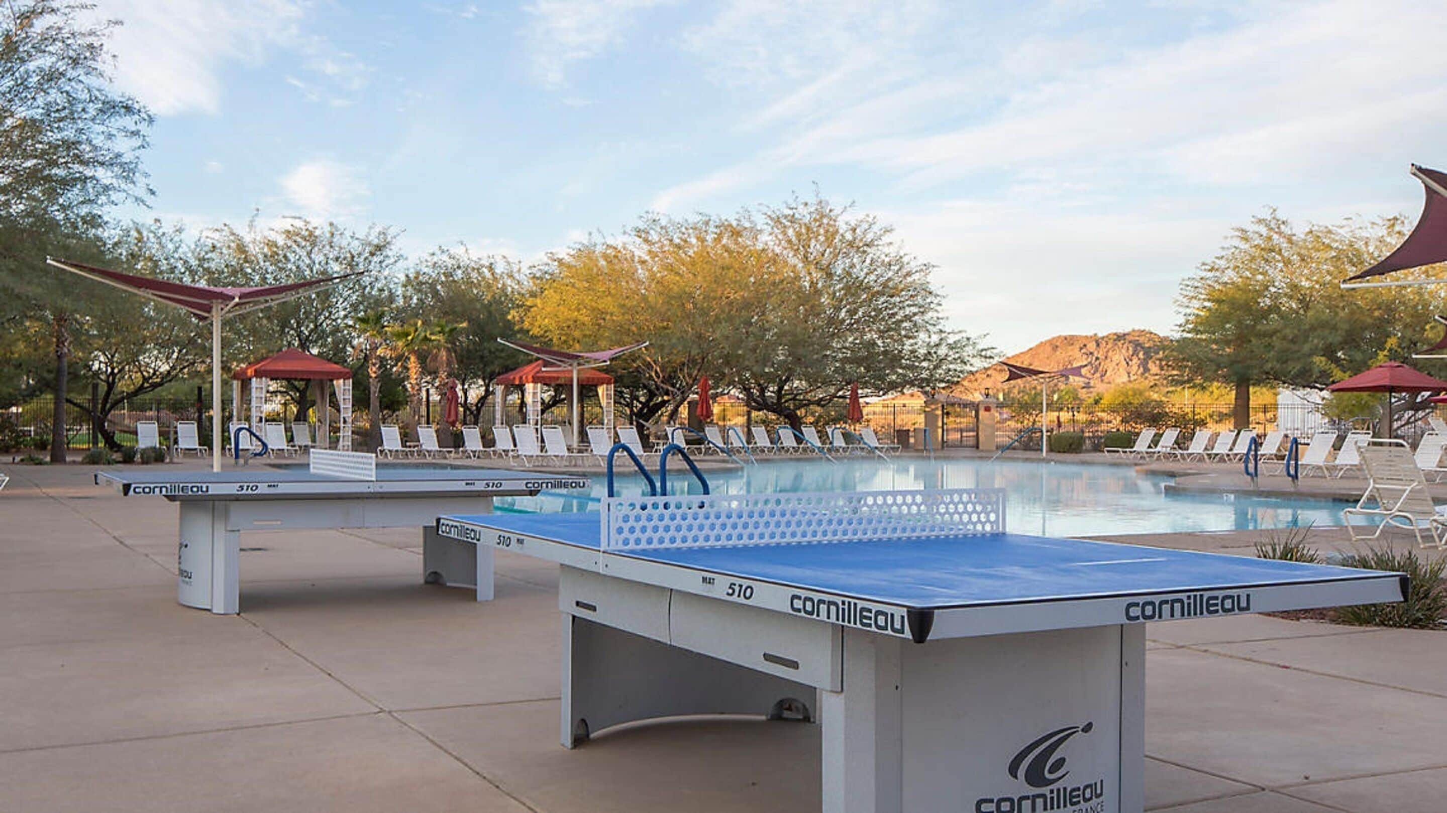 A pool area with a table tennis table, lounge chairs, and umbrellas.