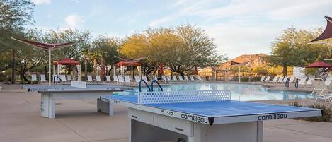 A pool area with a table tennis table, lounge chairs, and umbrellas.