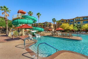 A swimming pool with a water slide, lounge chairs, and palm trees.