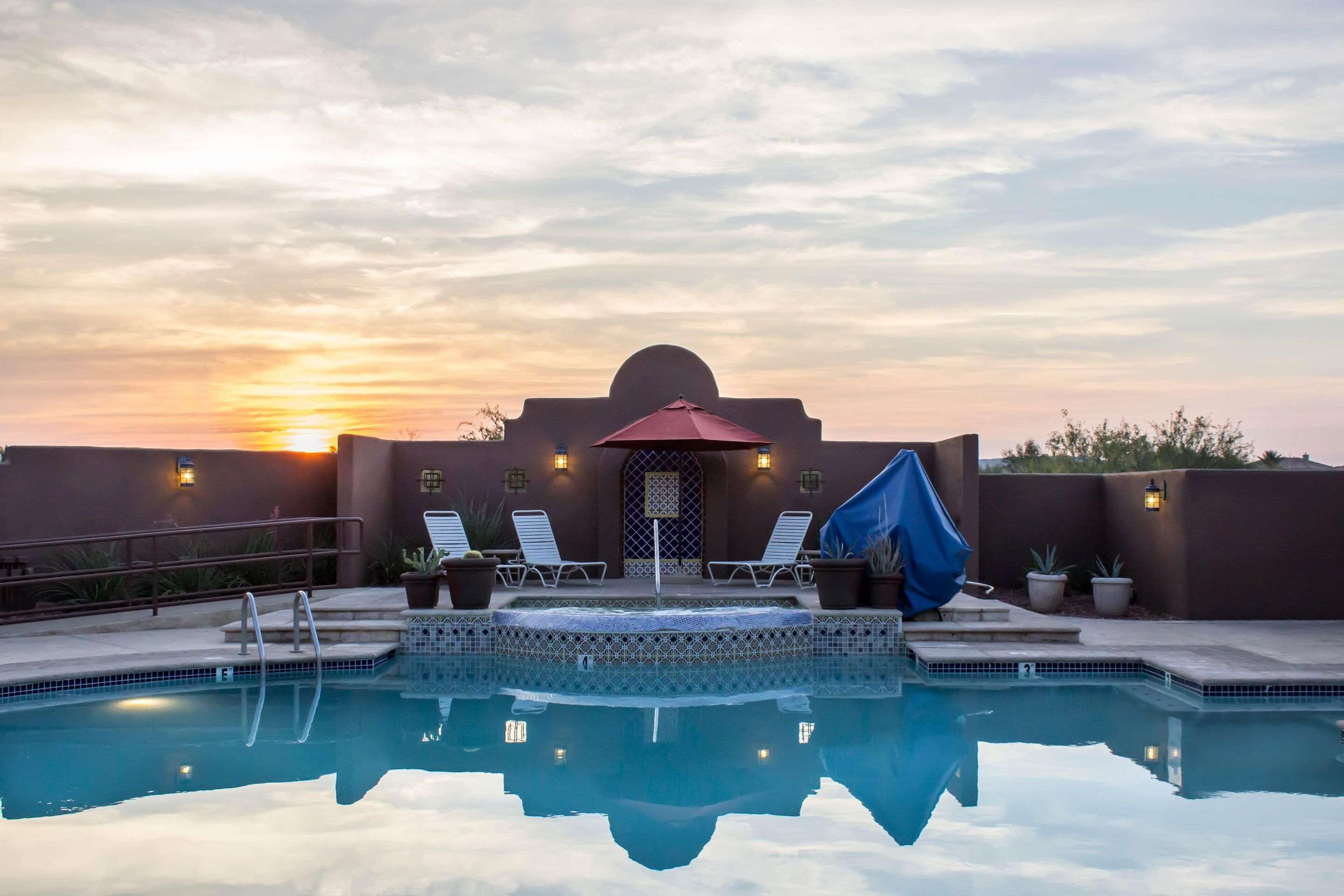 A pool area with lounge chairs and a covered seating area, reflecting the sunset in the background.