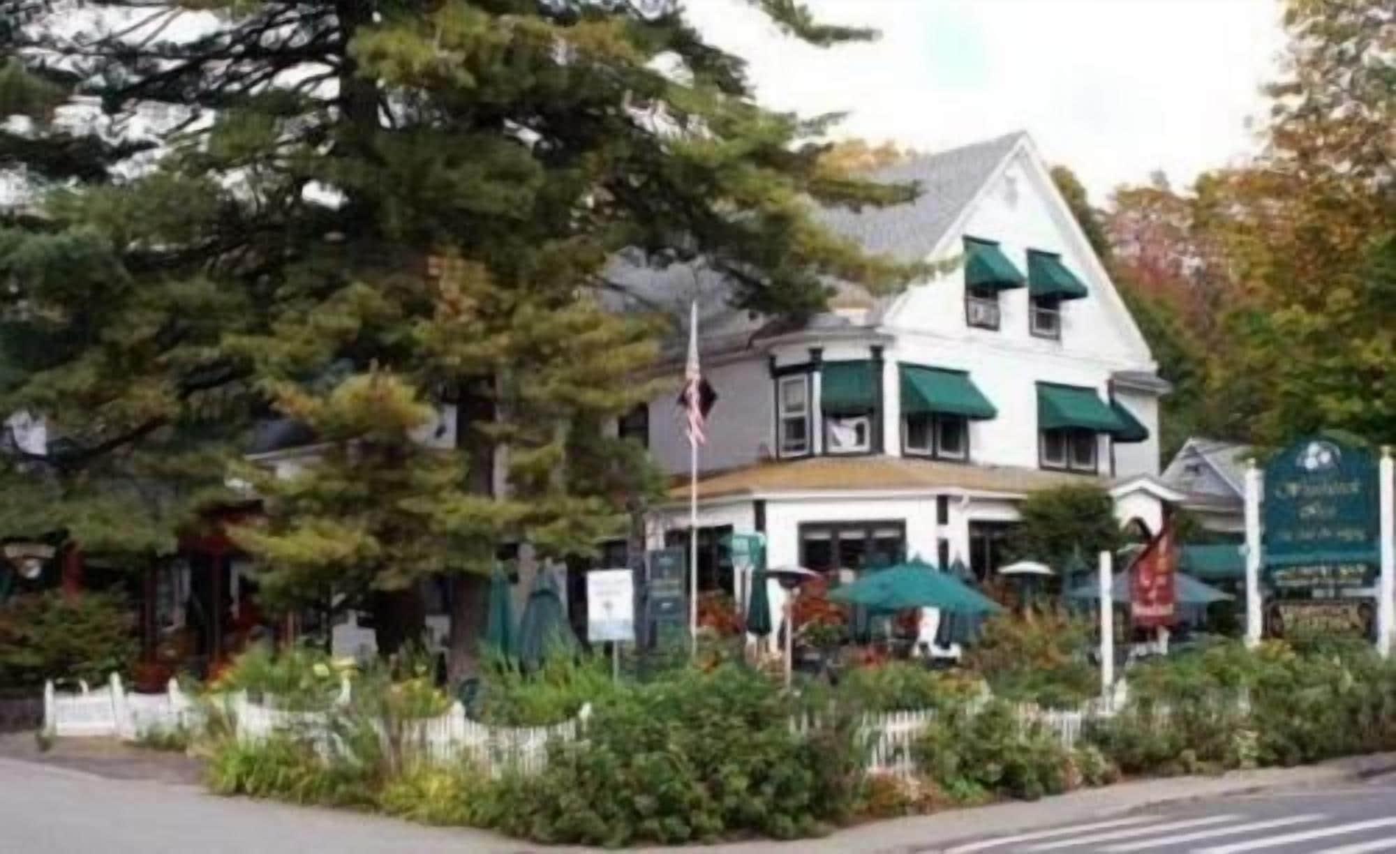 A two-story building with a white facade and green awnings, surrounded by greenery and a white fence.
