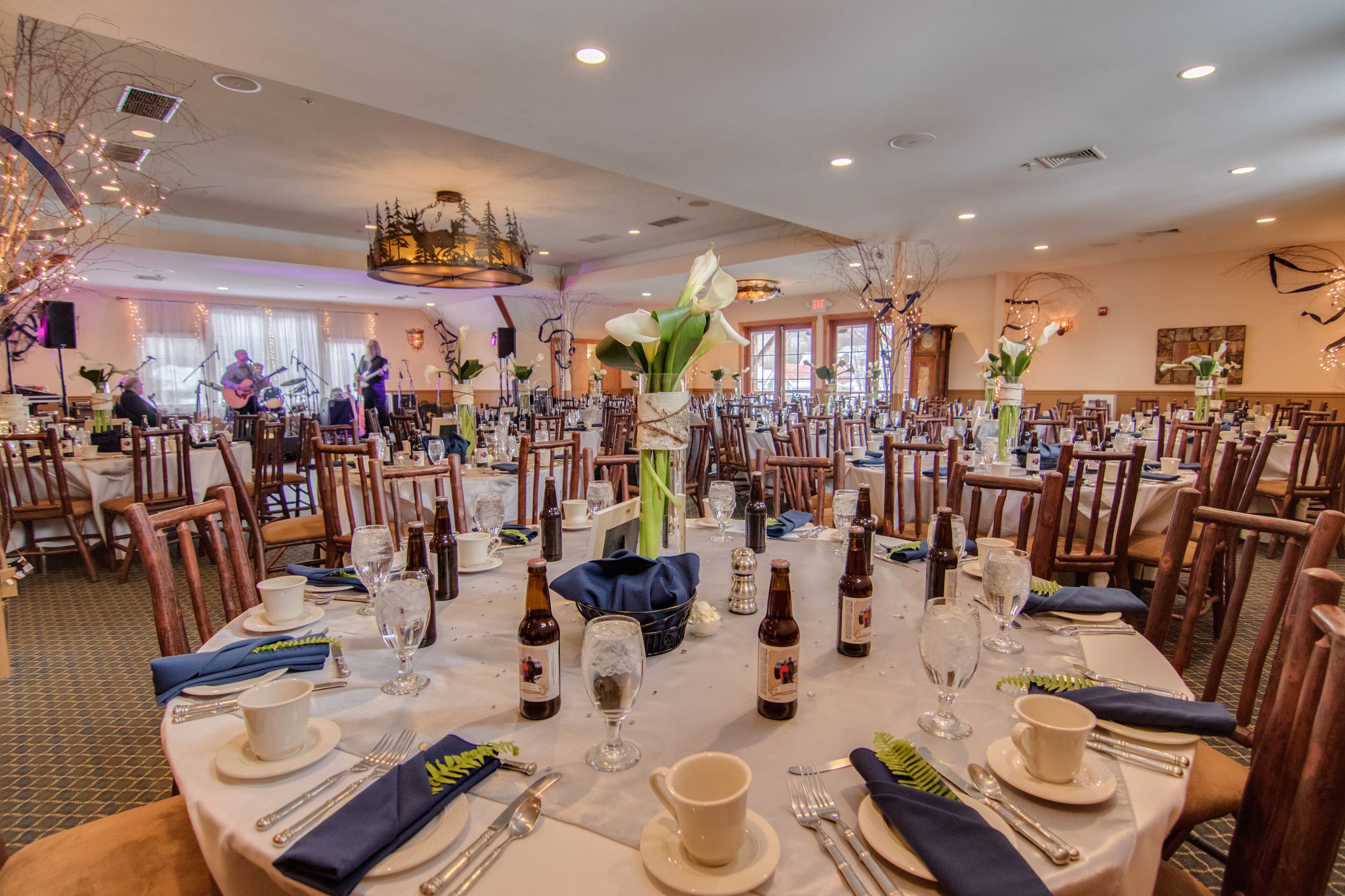 A banquet hall with round tables set for a formal event, complete with table settings, chairs, and a band performing in the background.