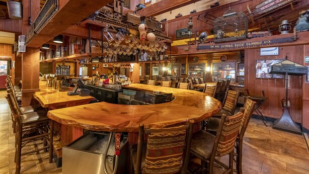 Un rústico espacio de bar con muebles de madera, una amplia barra y una variedad de botellas y vasos.