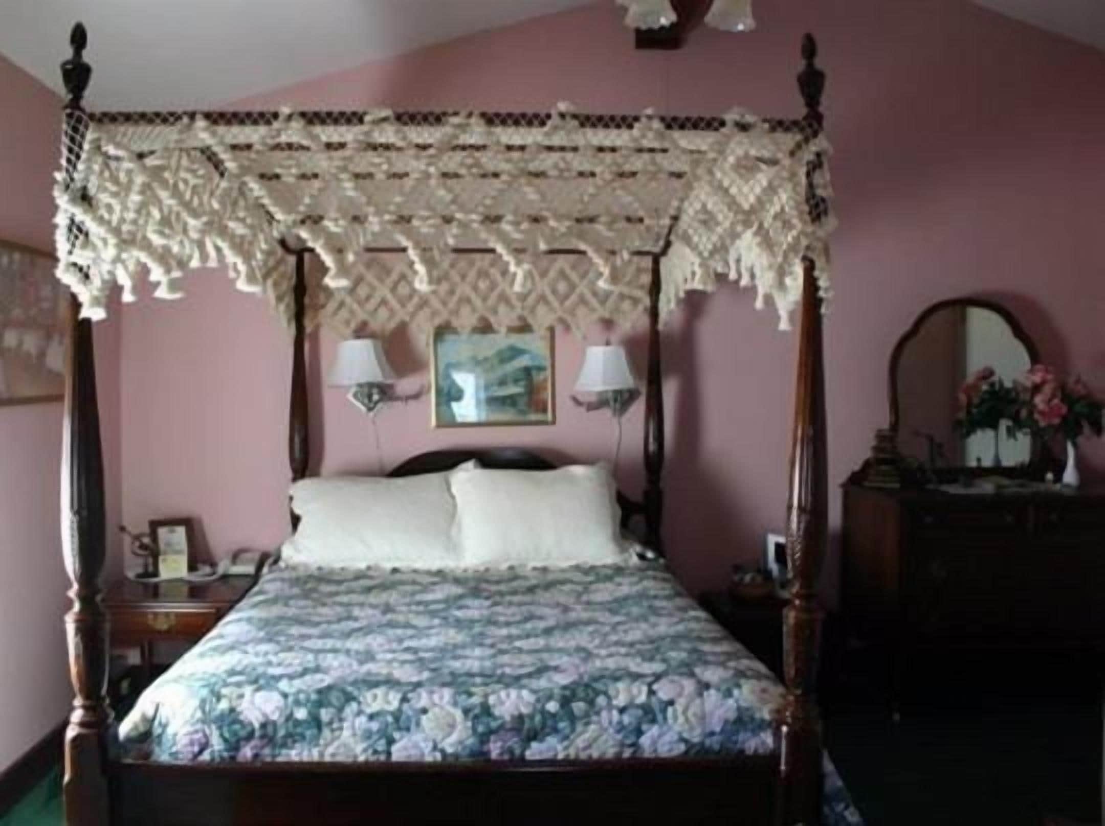 A four-poster canopy bed with a floral bedspread, bedside lamps, and a nightstand with a telephone.