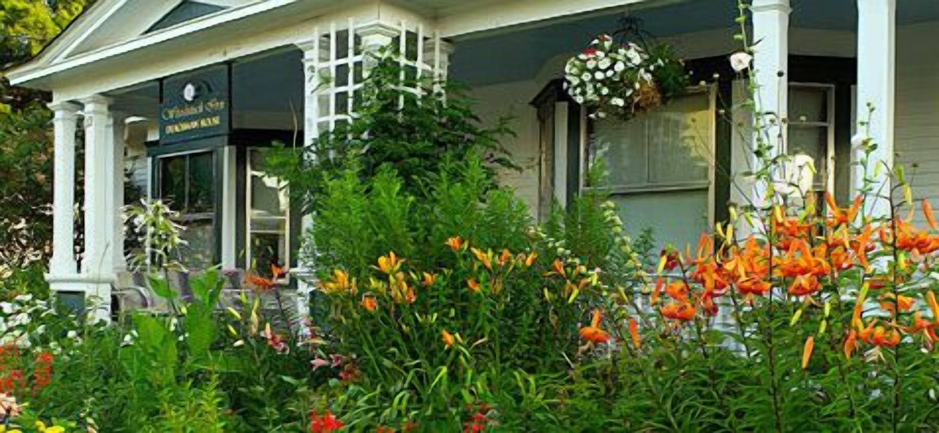Ein Gebäude mit einer Veranda, einem Schild mit der Aufschrift 'Charming Inn' und verschiedenen Blumen im Vordergrund.