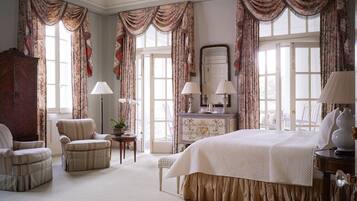 Une chambre spacieuse avec un grand lit, deux fauteuils, une commode et un miroir.