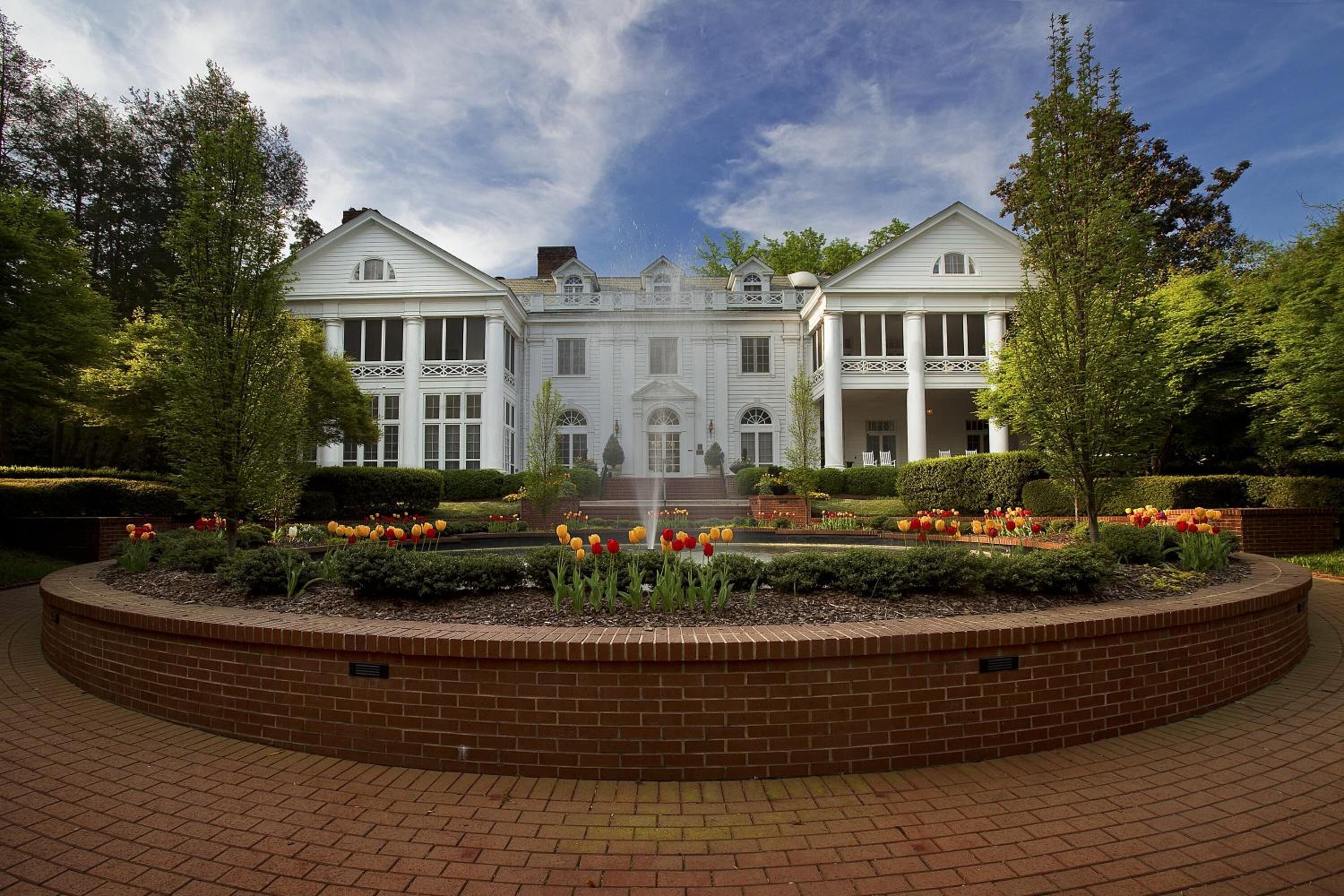 A large, symmetrical building with a central entrance, surrounded by a brick circular driveway and a well-maintained garden with tulips.