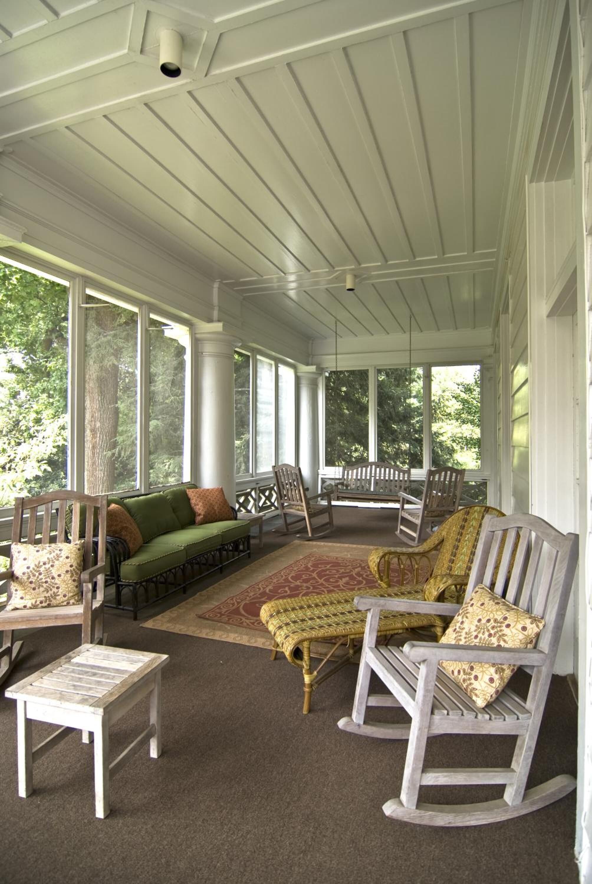A covered porch with a green sofa, rocking chairs, and a small table.