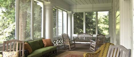 A covered porch with a green sofa, rocking chairs, and a small table.