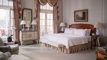 A classic hotel room with a large bed, two bedside tables with lamps, a dresser, a chair, and a window with curtains.