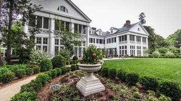 A large, white colonial-style building with multiple windows and a well-maintained garden with a central flower bed.
