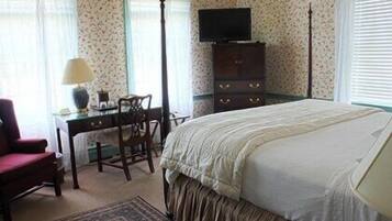 A bedroom with a bed, a desk with a chair, a dresser, and a television on the wall.