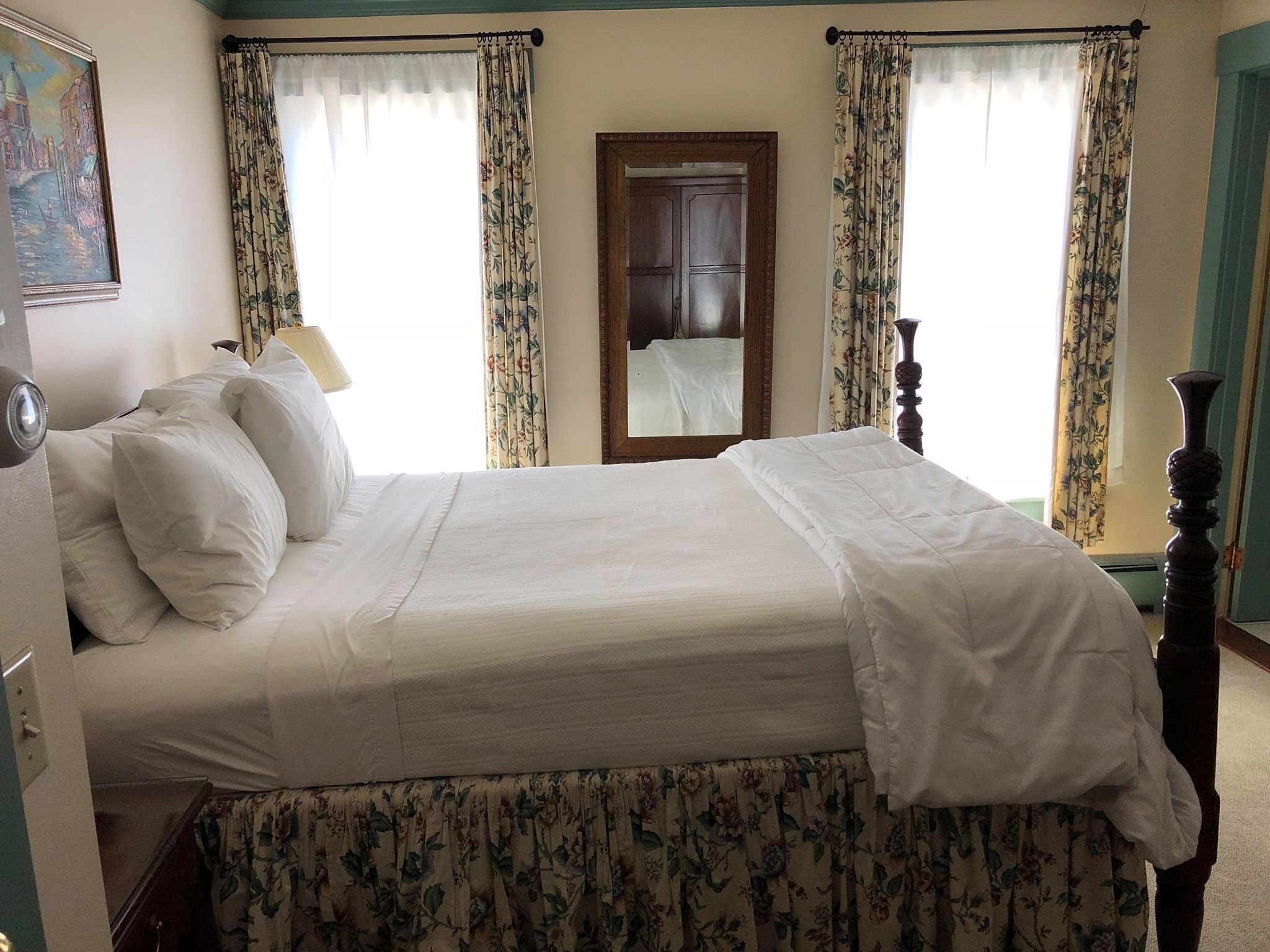 A neatly made bed with floral curtains, a wooden headboard, and a mirror above the door.