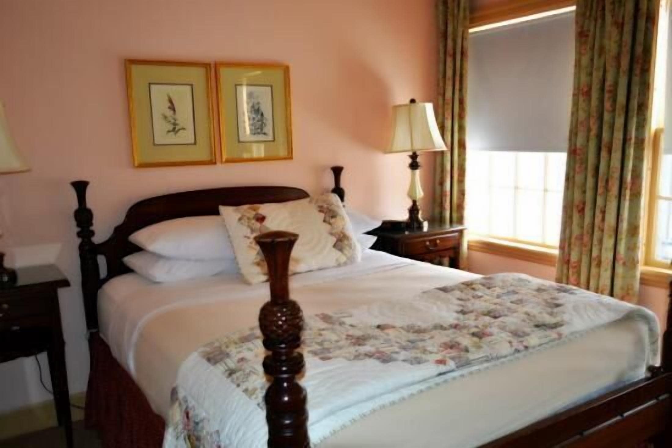 A bedroom with a wooden bed, a bedside table with a lamp, and two framed pictures on the wall.