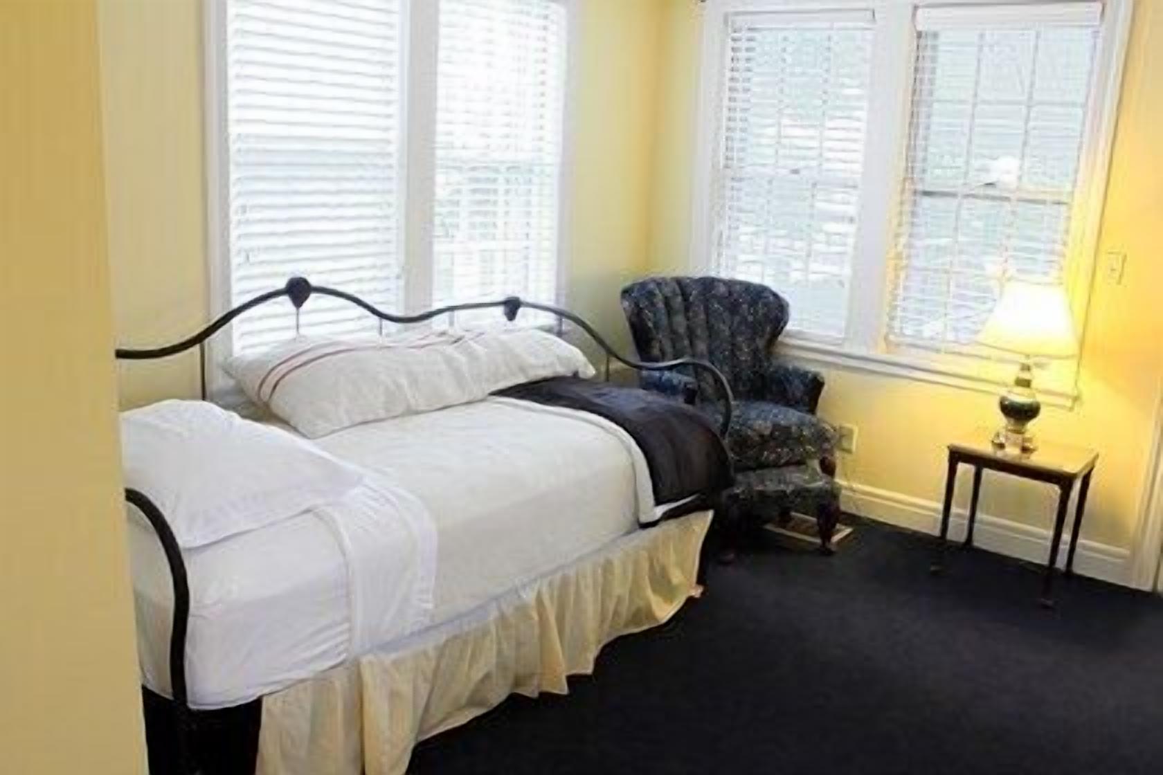 Un dormitorio con cama, una silla y una mesita de noche con lámpara.
