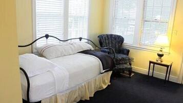 A bedroom with a bed, a chair, and a nightstand with a lamp.
