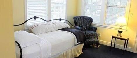 Un dormitorio con cama, una silla y una mesita de noche con lámpara.